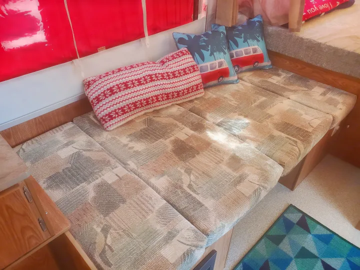 Interior of an RV rental: a compact living area with multi-patterned cushions forming a bench, decorated with red and camper van pillows.. Viking 1906st 2004