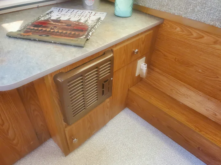 Cozy RV rental interior: counter with 'Welcome to the Camper' sign, wood cabinetry, furnace vent, outlet, and floor with steps.. Viking 1906st 2004