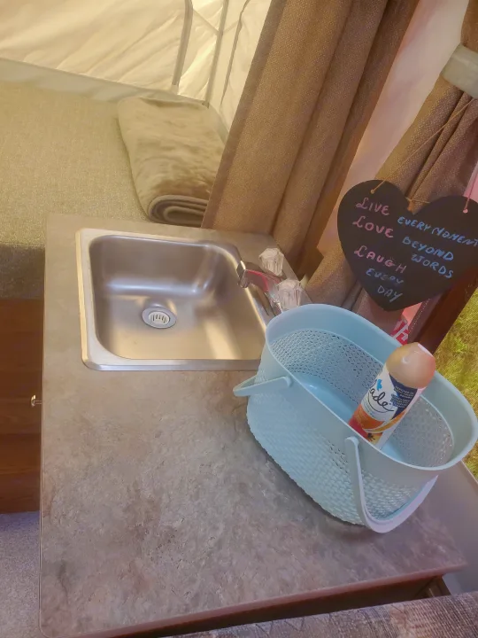 Cozy RV rental interior with a compact sink, countertop, and plush bed. Features an inspirational heart sign and air freshener.. Viking 1906st 2004