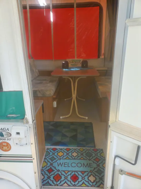 Inside a cozy RV rental: dining area with patterned cushions, a table, and welcome mats by the entry.. Viking 1906st 2004