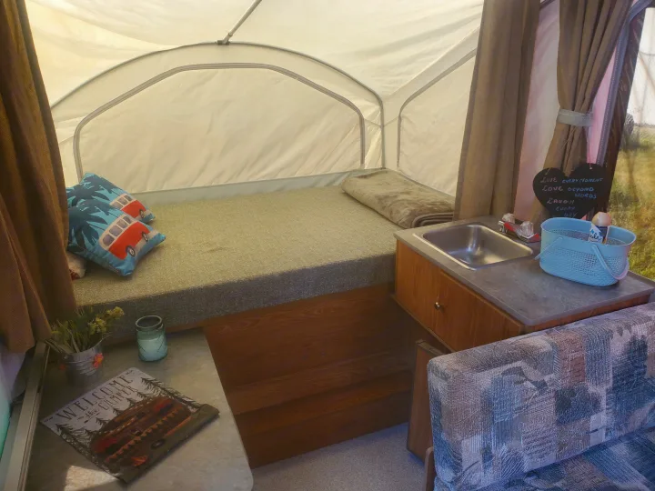 Inside a cozy RV rental: bed with pillows, compact sink, and homey camping decor like a welcome mat and sign.. Viking 1906st 2004