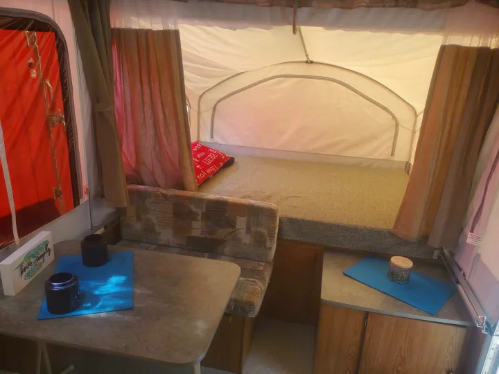 RV rental interior: pop-up camper with bed, dinette, and "live simply" sign. Your cozy camping experience awaits!. Viking 1906st 2004