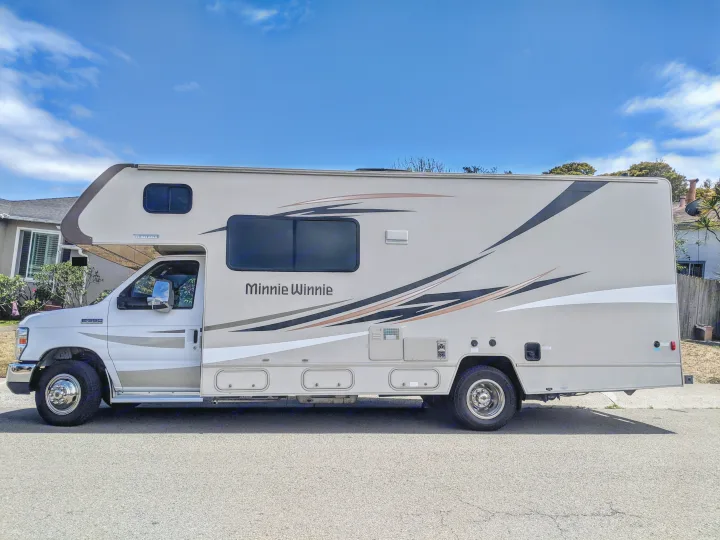 Side view of a beige Winnebago Minnie Winnie RV rental parked on asphalt under a blue sky.. Winnebago Minnie Winnie 2016