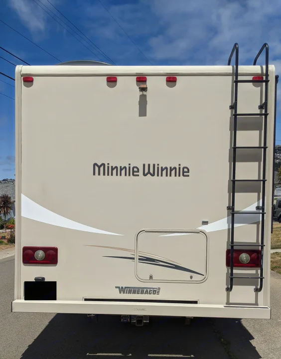 A beige "Minnie Winnie" Winnebago RV rental is shown from the rear, featuring a ladder, tail lights, and a hitch.. Winnebago Minnie Winnie 2016