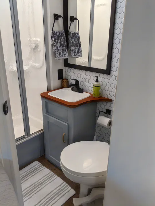 Compact RV rental bathroom: light gray vanity with wood top, white sink, black faucet, hexagonal wall tiles, modern shower, and toilet.. Winnebago Minnie Winnie 2016