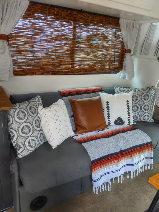 Cozy RV rental interior featuring a dark gray couch, patterned throw pillows, a vibrant blanket, and bamboo window blinds.. Winnebago Minnie Winnie 2016