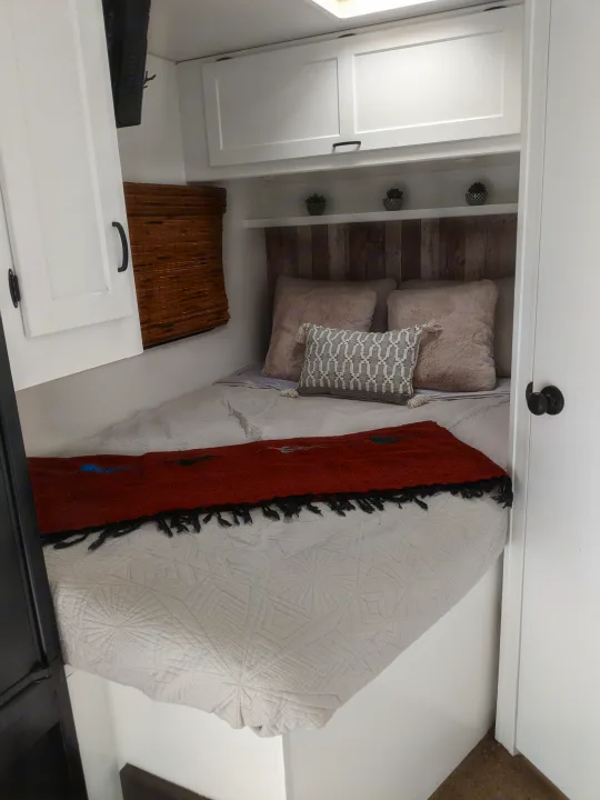 Cozy RV rental bedroom featuring a bed with a rustic headboard, soft bedding, and overhead storage, ideal for comfortable travel.. Winnebago Minnie Winnie 2016