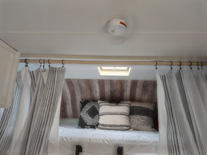 Cozy RV rental bedroom interior with striped curtains, patterned pillows, rustic wood paneling, and a skylight above the bed.. Winnebago Minnie Winnie 2016