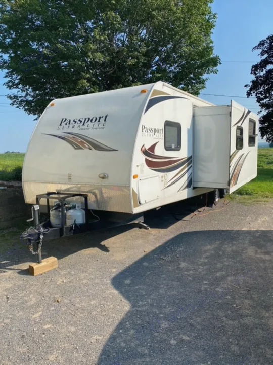 White Passport Ultralite travel trailer for RV rental, parked outside on a sunny day with visible propane tanks.. Other Passport 2012