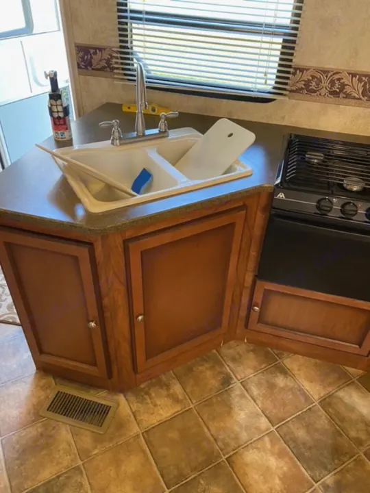 RV rental kitchen: Galley with a double sink, gas stovetop, wood cabinets, and tile floor. Window with blinds provides light.. Other Passport 2012