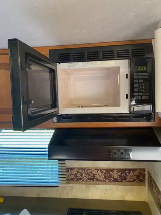 Clean, open microwave in an RV rental kitchen. Black appliance, digital display, compact setup next to a fridge.. Other Passport 2012