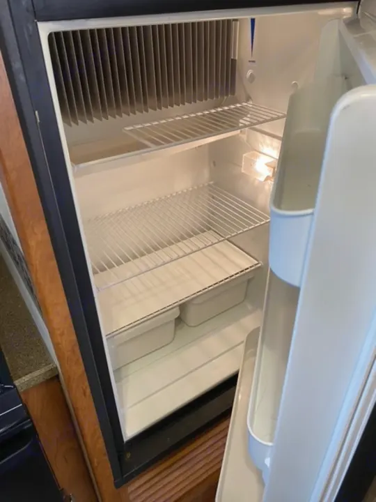 Spotless and empty RV rental refrigerator interior, featuring wire shelves, storage bins, and cooling fins, ready for use.. Other Passport 2012