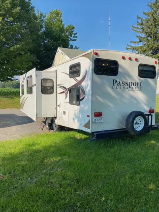 White Passport Ultralite travel trailer, an RV rental, parked outdoors on grass. Explore with this comfortable camper.. Other Passport 2012
