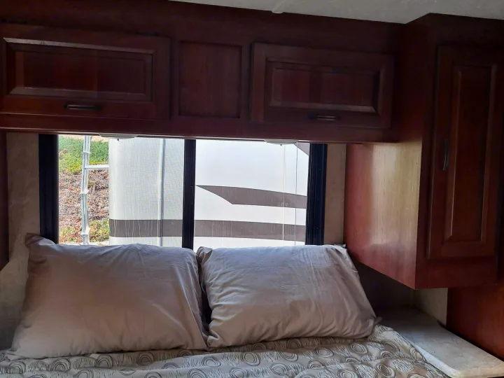 Cozy RV rental bedroom featuring wood cabinets, window views, and a comfortable bed setup.. Forest River Sunseeker 2018