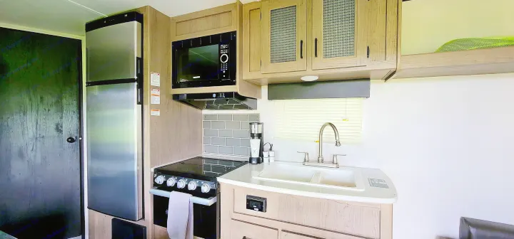This RV rental features a compact, modern kitchen with a fridge, microwave, stove, sink, and wood-look cabinets.. Keystone Hideout 2021