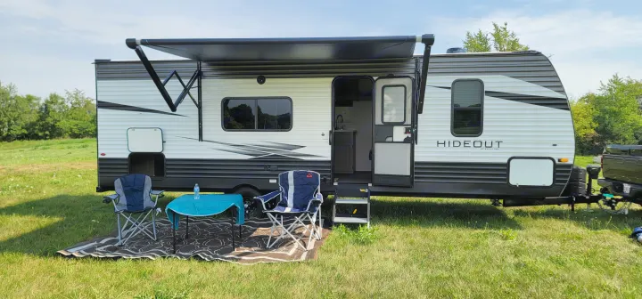 A travel trailer RV rental, parked on grass with an extended awning, chairs, and a table set up for outdoor relaxation.. Keystone Hideout 2021