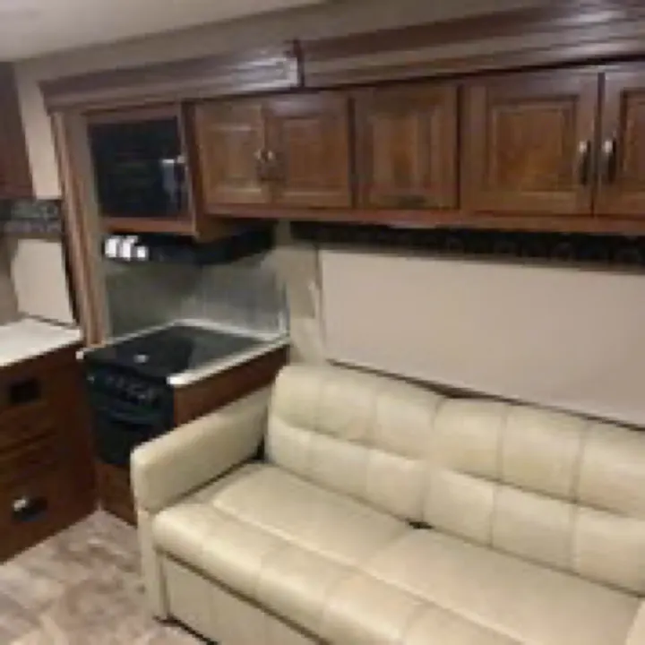 This RV rental interior features a compact kitchen with a stove, microwave, and cabinets, plus a cozy cream-colored sofa.. Forest River Sunseeker 2017