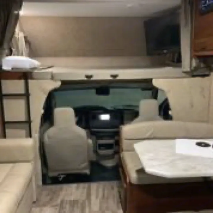 View inside an rv rental, showing the driver's cab, a large overhead bunk with TV, and a cozy dinette seating area.. Forest River Sunseeker 2017