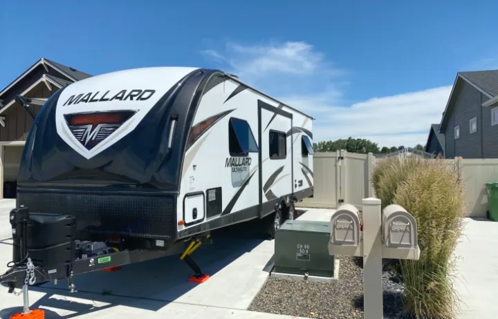 A white/black Mallard Ultralite travel trailer, a modern RV rental option, is parked on a residential driveway.. Heartland Other 2018