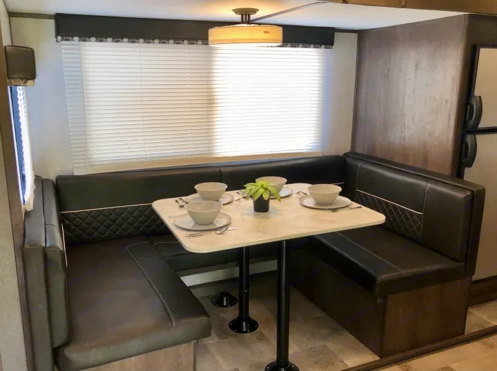 Modern RV rental dinette area featuring L-shaped black leather seating, white table, window, and overhead light.. Coleman Other 2021