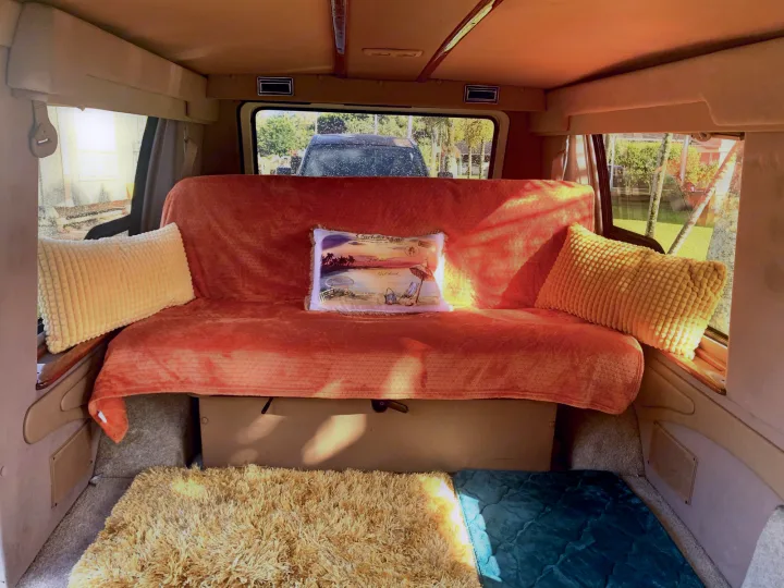 Cozy RV rental interior featuring an orange bench bed with pillows and soft floor mats, ready for travel adventures.. Dodge Ram 1500 1999