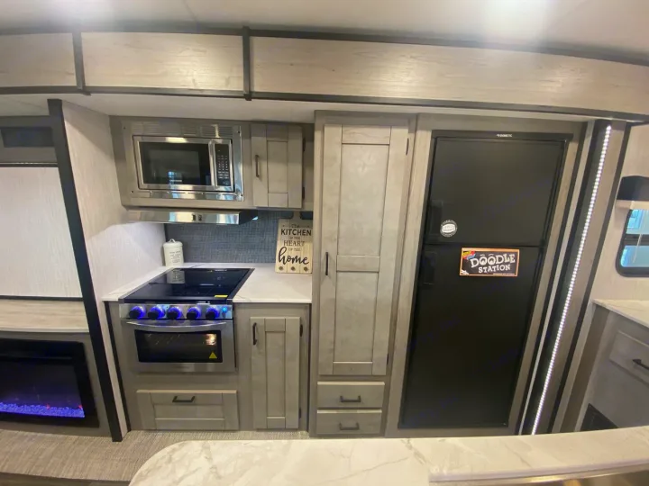 Modern RV rental kitchen featuring a microwave, stove, fridge, and cozy fireplace.. Heartland RVs Mallard 2021