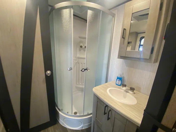 RV rental bathroom showing a compact space with a curved, frosted glass shower, vanity sink, and mirror cabinet.. Heartland RVs Mallard 2021