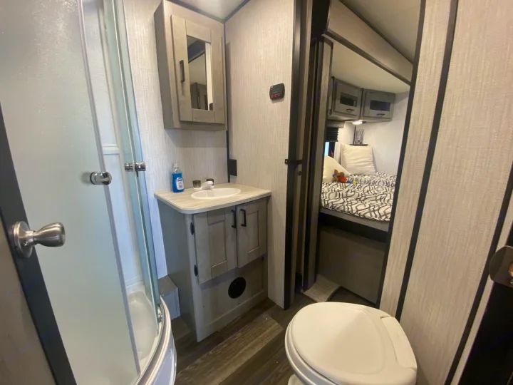 Inside an RV rental: a compact bathroom with shower, sink, toilet, and a view into the cozy bedroom.. Heartland RVs Mallard 2021