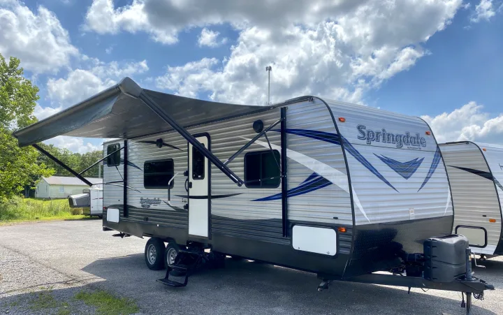 Spacious Springdale travel trailer, ideal for RV rental, with an extended awning. Parked outdoors under a blue, cloudy sky.. Keystone Springdale 2018