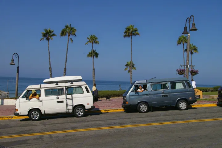 Coastal RV rental trip: Two vintage VW camper vans by the sunny ocean with palm trees.. Volkswagen Westfalia 1986