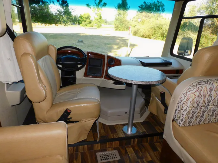 This RV rental features a spacious beige cockpit with a steering wheel, comfy seats, and a small table setup.. Coachmen Pursuit 2017