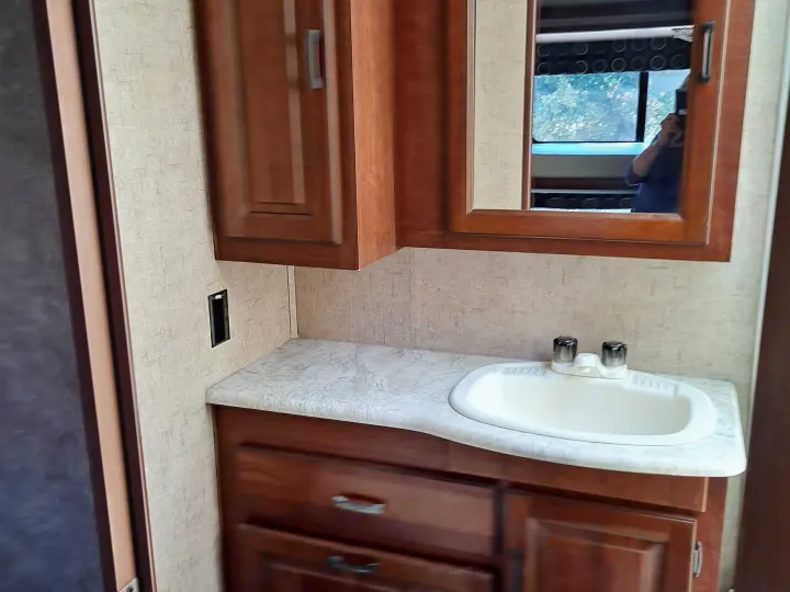 Inside an RV rental: a compact bathroom vanity with a sink, mirror, and wooden cabinets.. Forest River Sunseeker 2018