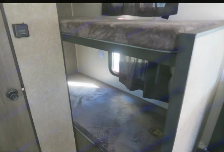 RV rental's cozy interior features comfortable bunk beds with dark mattresses. A window with curtains provides natural light to the lower bunk.. Highland Ridge RV Open Range 2021