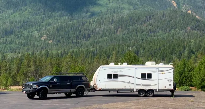 Black truck towing a white Arctic Fox travel trailer, an ideal RV rental for exploring forested mountains.. Northwood Mfg Arctic Fox 2013