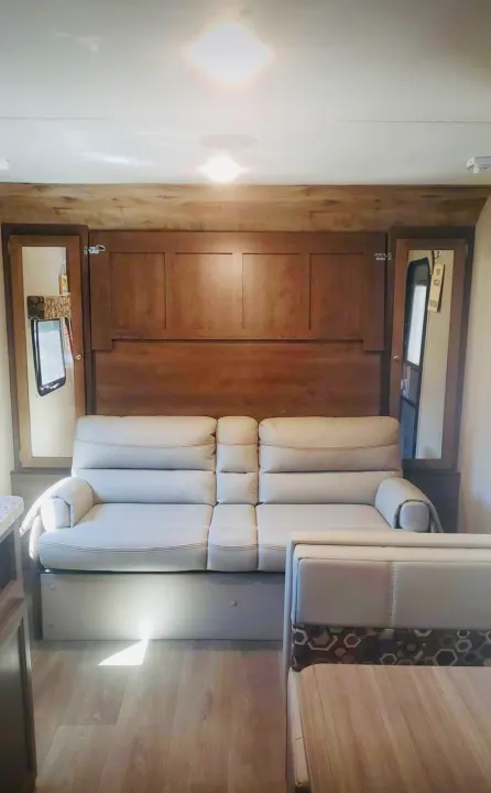 View of a modern rv rental living area: light-colored sofa, wood paneling, and dinette, suggesting a comfortable, adaptable space.. Dutchmen Other 2018