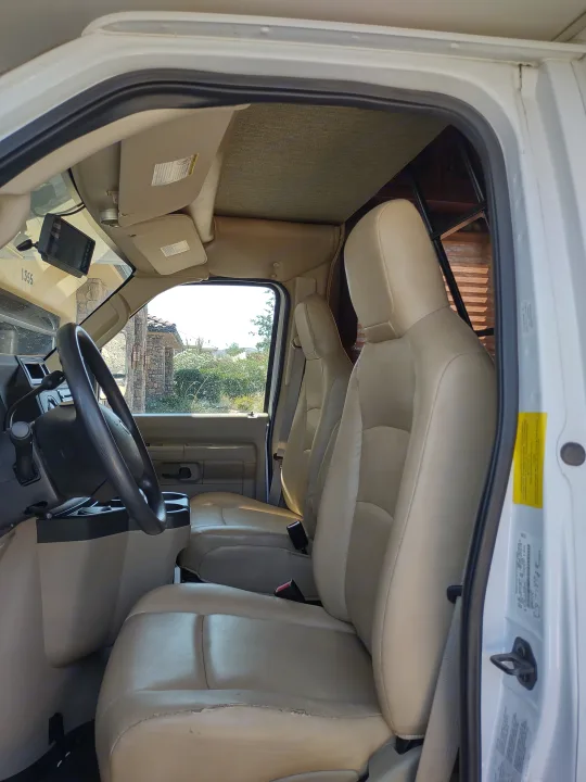 RV rental interior, showing the driver's cab, light beige seating, and overhead bunk. Some seat wear visible.. Forest River Sunseeker 2012