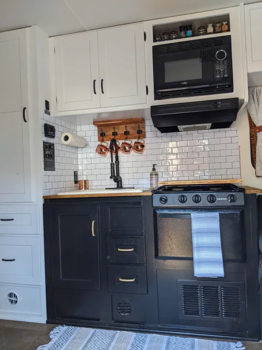 Stylish RV rental kitchen with white and black cabinets, subway tile, and a full oven/range, ideal for mobile cooking.. Winnebago Minnie Winnie 2016