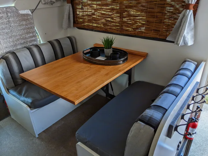 An inviting **RV rental** dinette setup: bright wooden table, striped cushions, and natural bamboo blinds create a cozy space.. Winnebago Minnie Winnie 2016