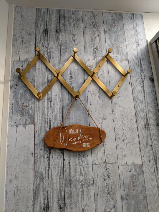 Compact storage for an rv rental: expandable brass coat rack with a travel-themed 'Wander' sign on rustic wood paneling.. Winnebago Minnie Winnie 2016