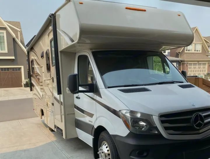 This white Mercedes-Benz Sprinter Class C RV rental awaits its next adventure, parked in a sunny driveway.. Coachmen Prism 2016
