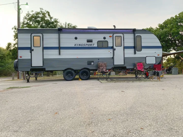 Grey travel trailer RV rental with purple awning lights, chairs, and a dog at a campsite.. Gulf Stream Kingsport 2021