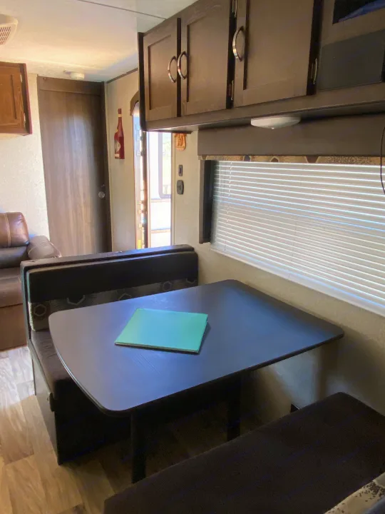 Cozy rv rental interior featuring a dinette with dark table and booth seating, overhead cabinets, and a window with blinds.. Keystone Springdale 2018