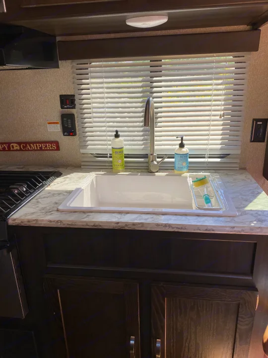 RV rental kitchen showcasing a clean sink with Mrs. Meyer's soaps, modern faucet, window blinds, and tank controls.. Keystone Springdale 2018