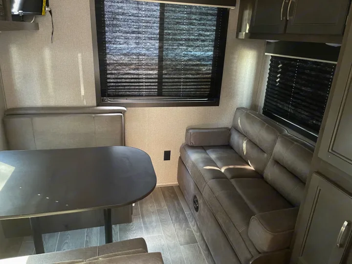 Inside a cozy RV rental: a dark table with bench seating, a comfy L-shaped sofa, and window blinds. Modern living space.. Jayco Baja 2021