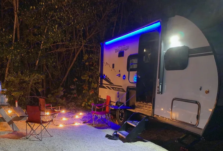 Illuminated RV rental with blue awning lights, surrounded by cozy ground lights, chairs, and a picnic table at a night campsite.. Forest River Cherokee Wolf Pup Black Label 2021
