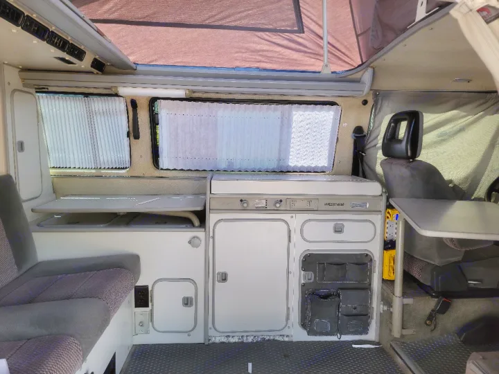 Spacious RV rental interior of a Westfalia pop-top camper, featuring a kitchenette, seating, and table setup.. Volkswagen Vanagon 1990