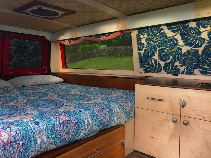 Cozy RV rental interior with bed, kitchen, and window view. Perfect for van life adventures.. Ford E150 2011