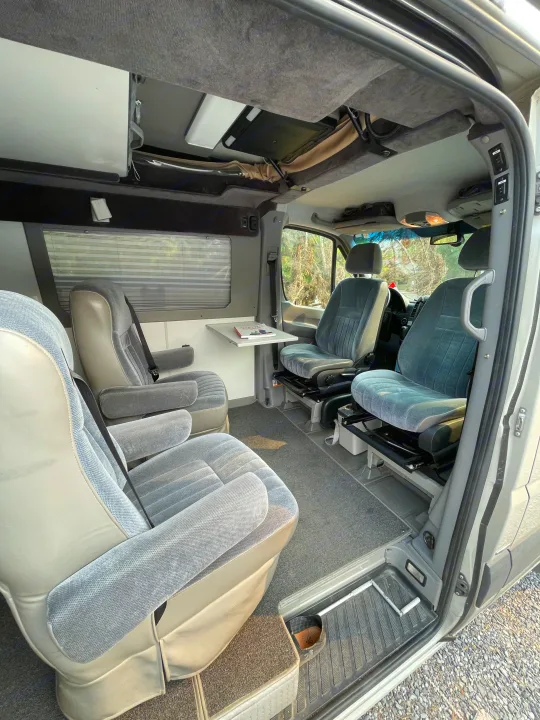 Step inside this RV rental! View of grey swivel captain's chairs, comfortable rear seating, and a side table in a clean, carpeted interior.. Sportsmobile Custom Design 2013