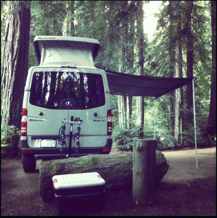 RV rental camper van with pop-top & awning in a tall forest campsite. Ideal for nature road trips.. Sportsmobile Custom Design 2013