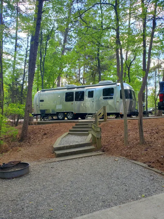 Silver Airstream RV rental at a wooded campsite with steps and fire pit.. Airstream Flying Cloud 2018